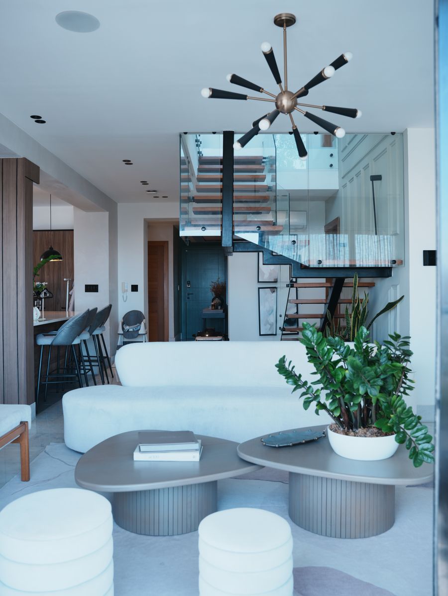 Pent-House Familiar en Renacimiento: sala terminada con sofá blanco, mesas redondas y escalera flotante de vidrio al fondo